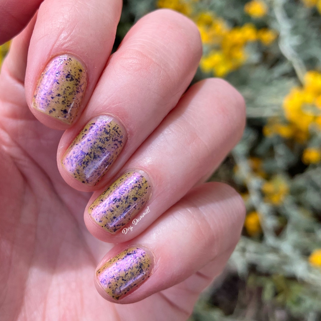The four fingers of Haylee's right hand hand with Emily de Molly's Lost Contact nail polish on the nails - a dirty yellow/green base with violet overlay and black flakes.